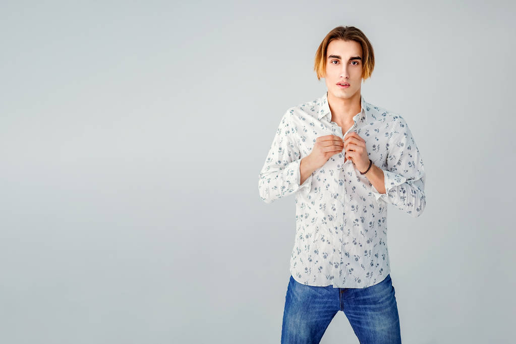 Mode portret van de jonge man in een wit overhemd houdingen over grijs muur - Foto, afbeelding