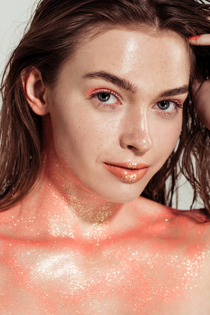 menina bonita com maquiagem brilho coral posando e olhando para a câmera isolada no cinza
 - Foto, Imagem