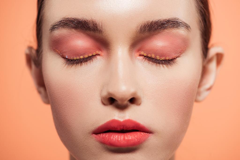 beautiful stylish young woman with glitter makeup and eyes closed isolated on coral - Photo, Image