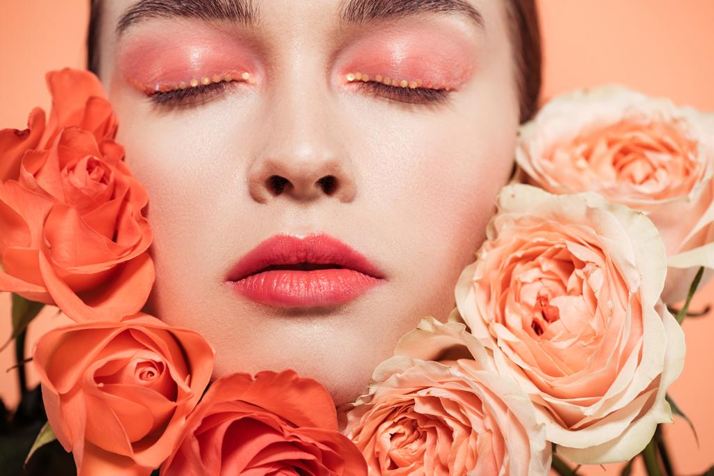 beautiful trendy girl posing with rose flowers and eyes closed isolated on coral - Photo, Image