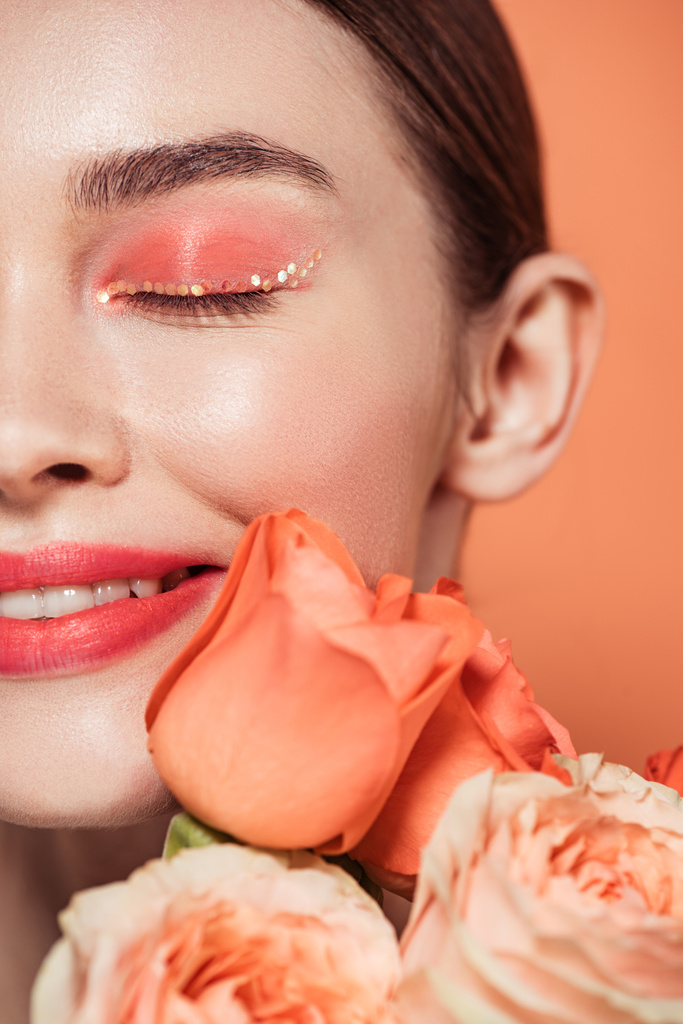 beautiful smiling stylish girl posing with eyes closed and rose flowers isolated on coral - Photo, Image