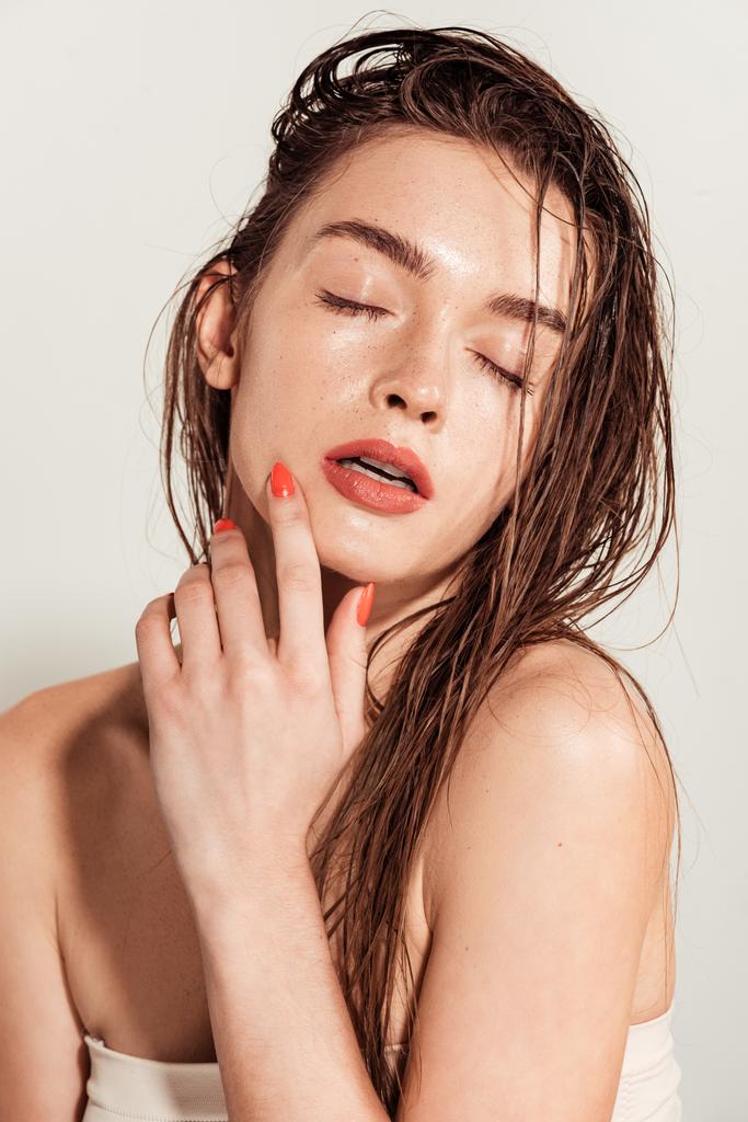 beautiful young woman with coral lips, eyes closed and wet hair posing isolated on grey - Photo, Image