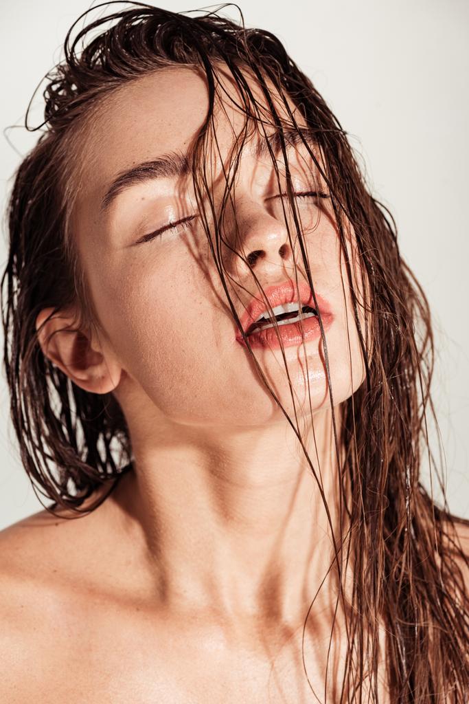 hermosa mujer joven seductora con labios de coral, los ojos cerrados y el pelo mojado posando aislado en gris
 - Foto, Imagen