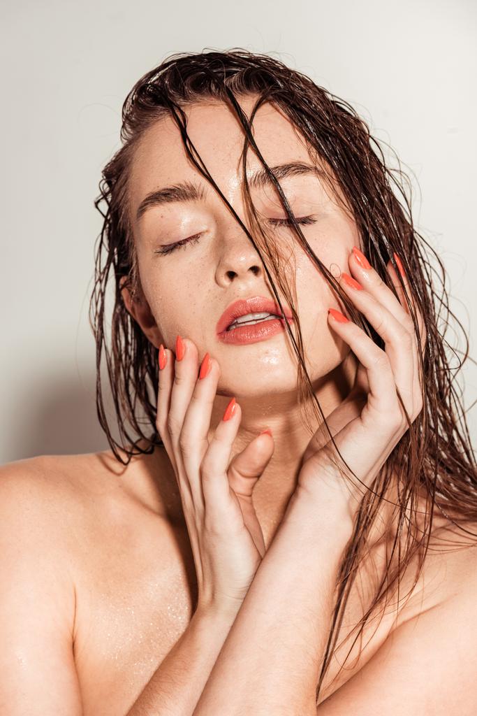 krásná mladá žena s korálové rty, oči zavřené a mokré vlasy dotýkání tváře na šedém pozadí - Fotografie, Obrázek