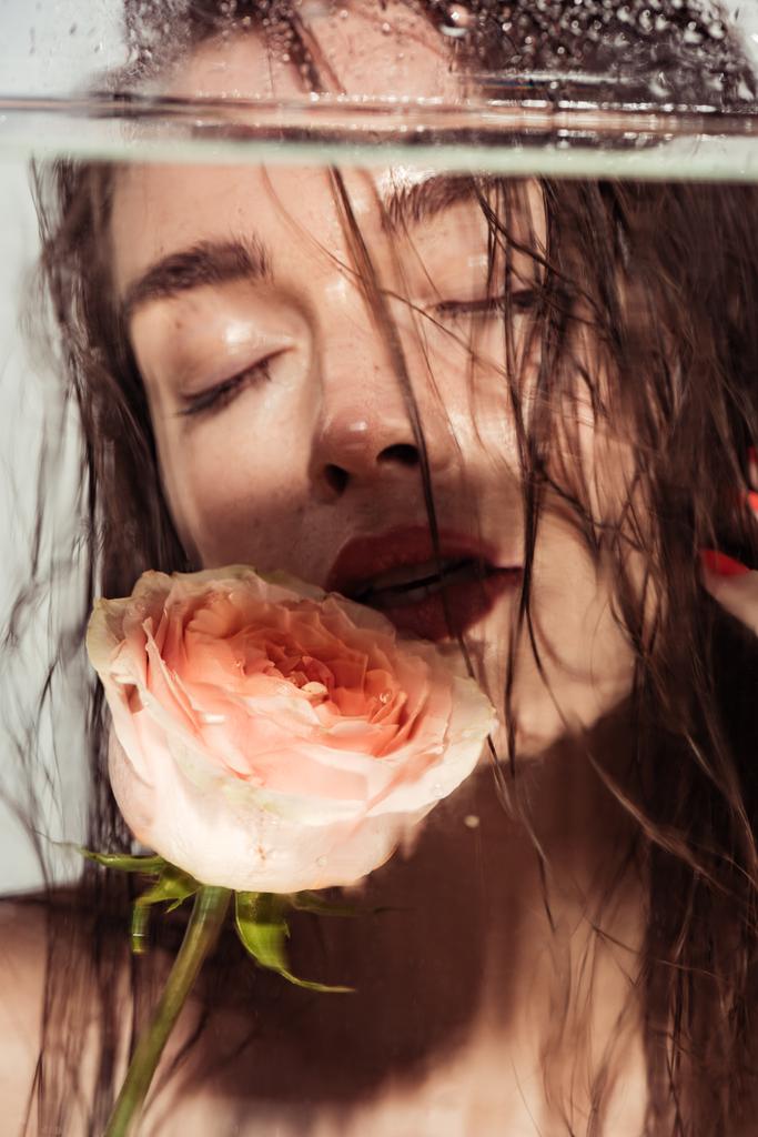 красива молода жінка з кораловими губами і трояндою квітка позує через акваріум ізольована на сірому
 - Фото, зображення
