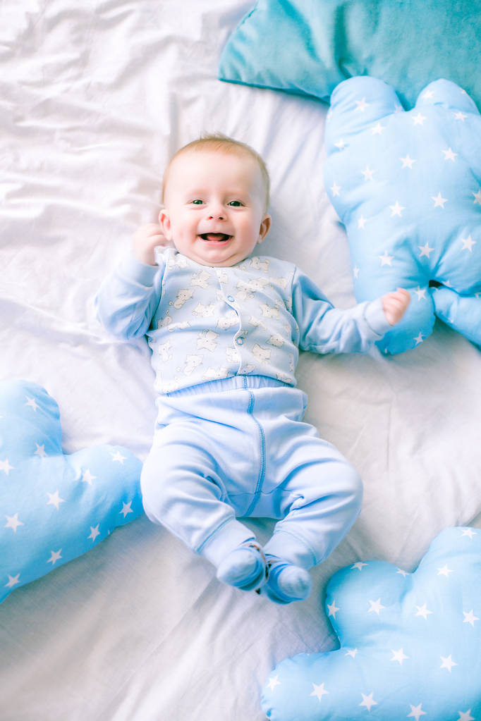 Lindo niño en la cama en casa rodeado de almohadas azules
 - Foto, imagen