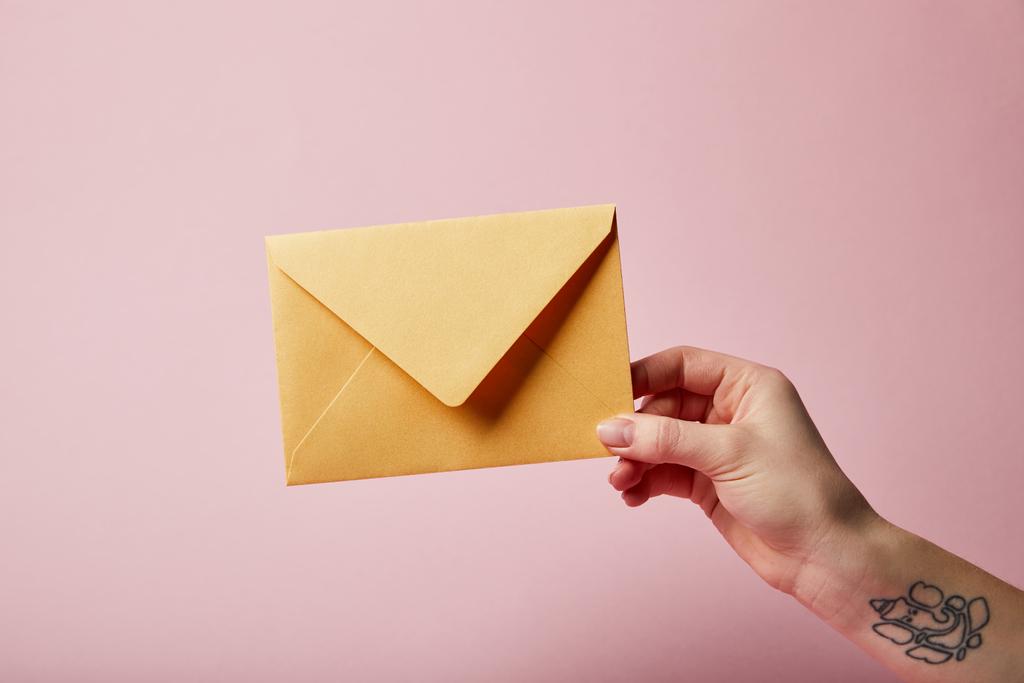 ピンクの背景に黄色の封筒を押しの入れ墨を持つ女性の部分的なビュー  - 写真・画像