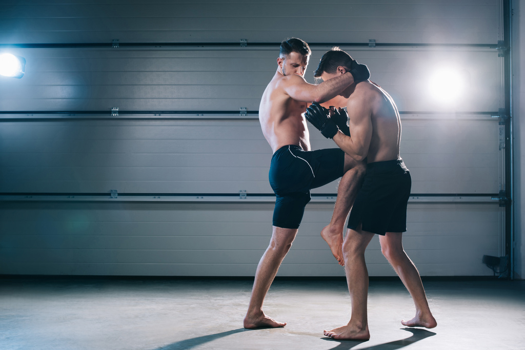 Widok z boku mięśni mma fighter kopiąc sportive przeciwnika w żołądku z kolana - Zdjęcie, obraz