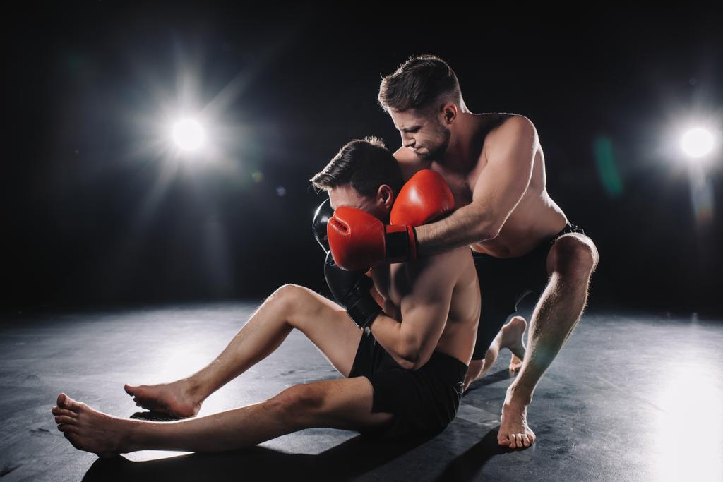 starke MMA-Kämpferin in Boxhandschuhen beim Würgen eines anderen Sportlers am Boden - Foto, Bild