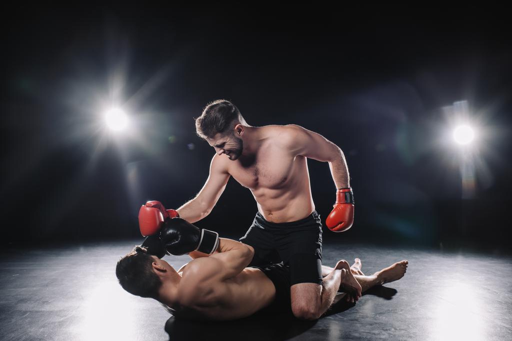 starke MMA-Kämpferin in Boxhandschuhen schlägt Gegner, während Sportler am Boden liegt - Foto, Bild