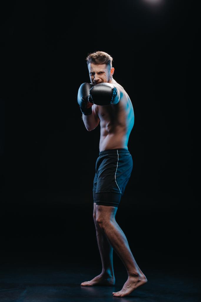 mięśni shirtless forsownych bokser robi cios na czarne rękawice bokserskie - Zdjęcie, obraz