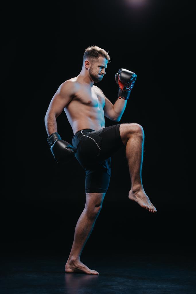 muskulöser, barfüßiger Boxer in Boxhandschuhen beim Kicken auf schwarz - Foto, Bild