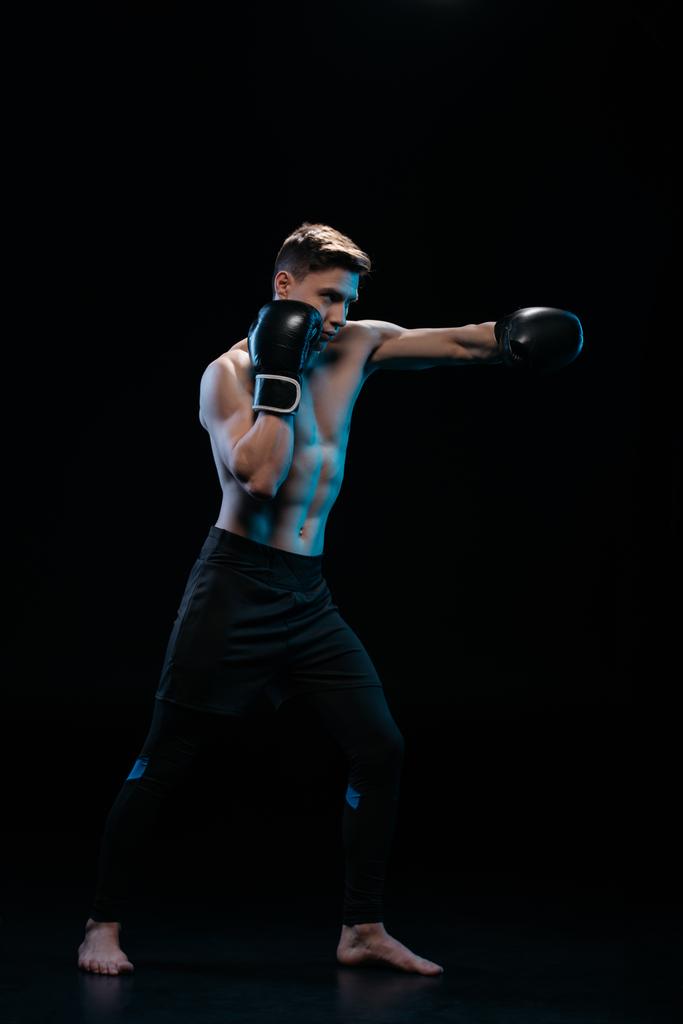 muscular fuerte descalzo mma luchador en guantes de boxeo haciendo ponche en negro
 - Foto, Imagen