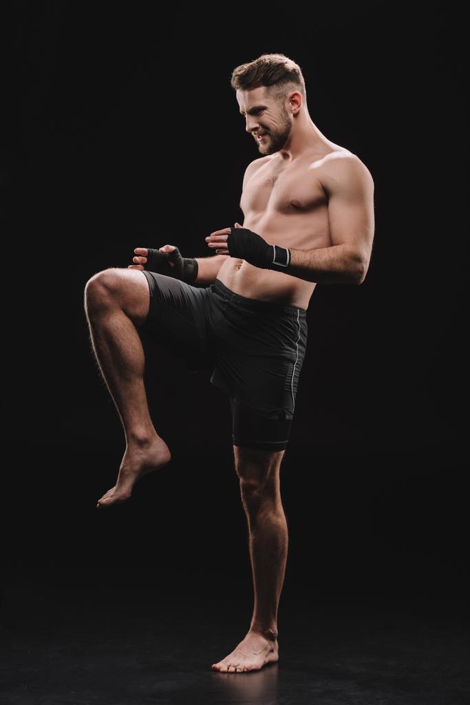 μυϊκή ξυπόλυτος ΜΜΑ μαχητής με γάζες κάνει kick με το γόνατο σε μαύρο - Φωτογραφία, εικόνα