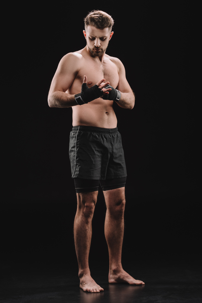 strong barefoot muscular mma fighter fixing bandages on black - Photo, Image
