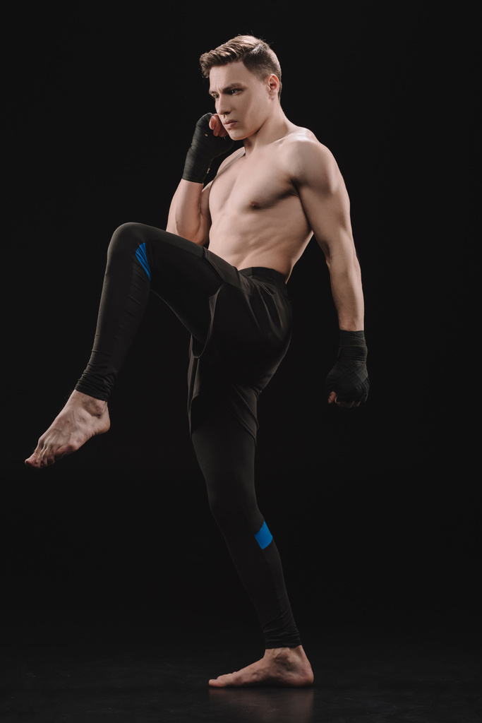 ισχυρή μυϊκή ξυπόλυτος αθλητή με γάζες κάνει kick σε μαύρο - Φωτογραφία, εικόνα