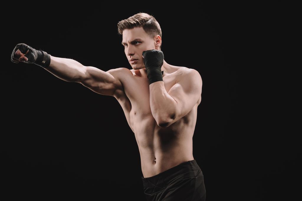 strong shirtless muscular sportsman in bandages doing punch isolated on black - Photo, Image