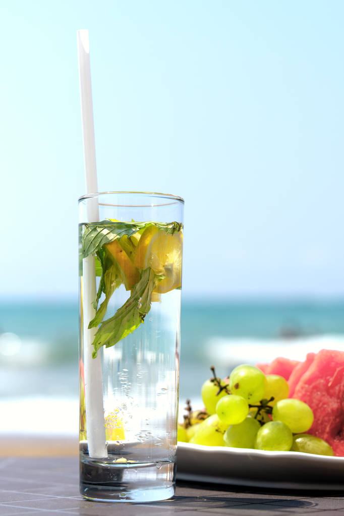 bir tabak meyve, sahilde, denize çerçevede bir masada cam limon içecek ve çirkin nane yaprakları - Fotoğraf, Görsel