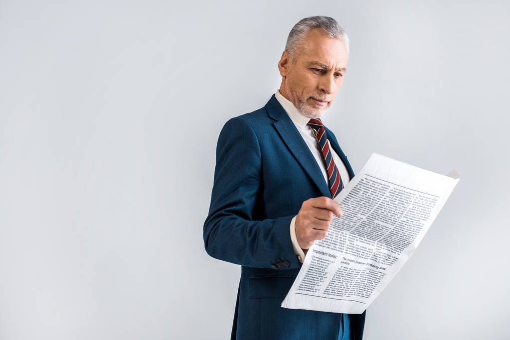 mature businessman reading newspaper while standing isolated on grey  - Photo, Image