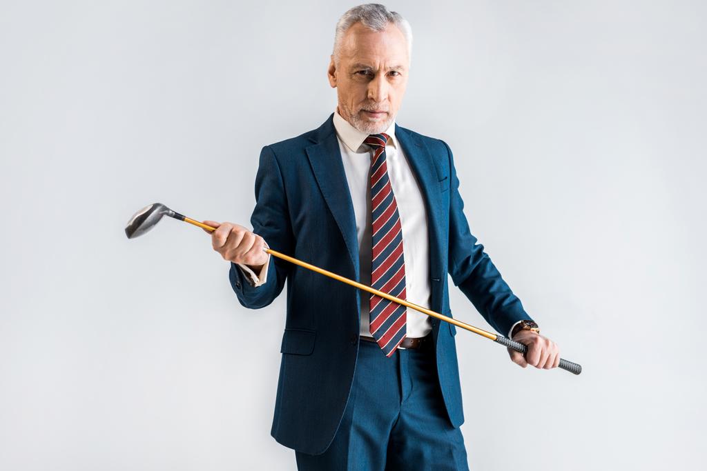 ernstige volwassen man in pak houden Golfclub geïsoleerd op grijs - Foto, afbeelding