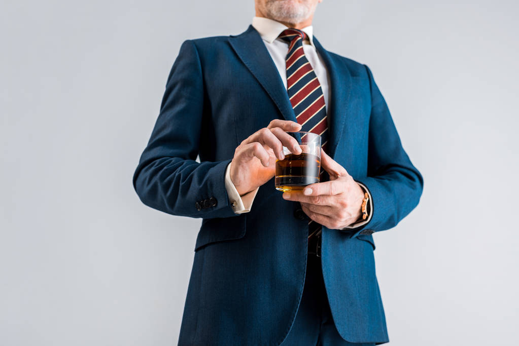 vista recortada de hombre de negocios maduro en traje sosteniendo vidrio con whisky aislado en gris
  - Foto, imagen
