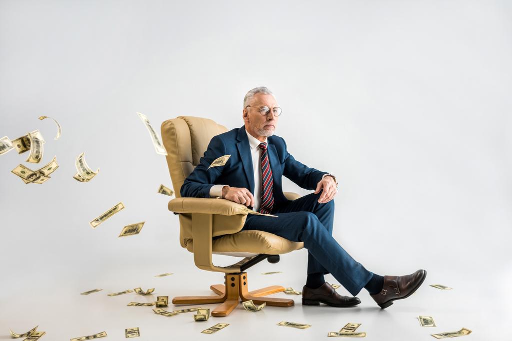 luottavainen kypsä liikemies istuu nojatuolissa lähellä dollarin setelien harmaa valikoiva painopiste
  - Valokuva, kuva