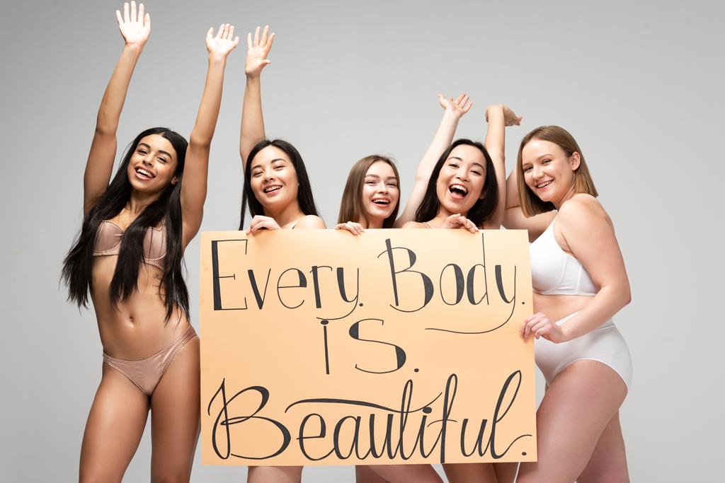 pięciu szczęśliwy dziewcząt wieloetnicznym gospodarstwa afisz z napisem "każde ciało jest piękne" i machanie rękami na szarym tle  - Zdjęcie, obraz