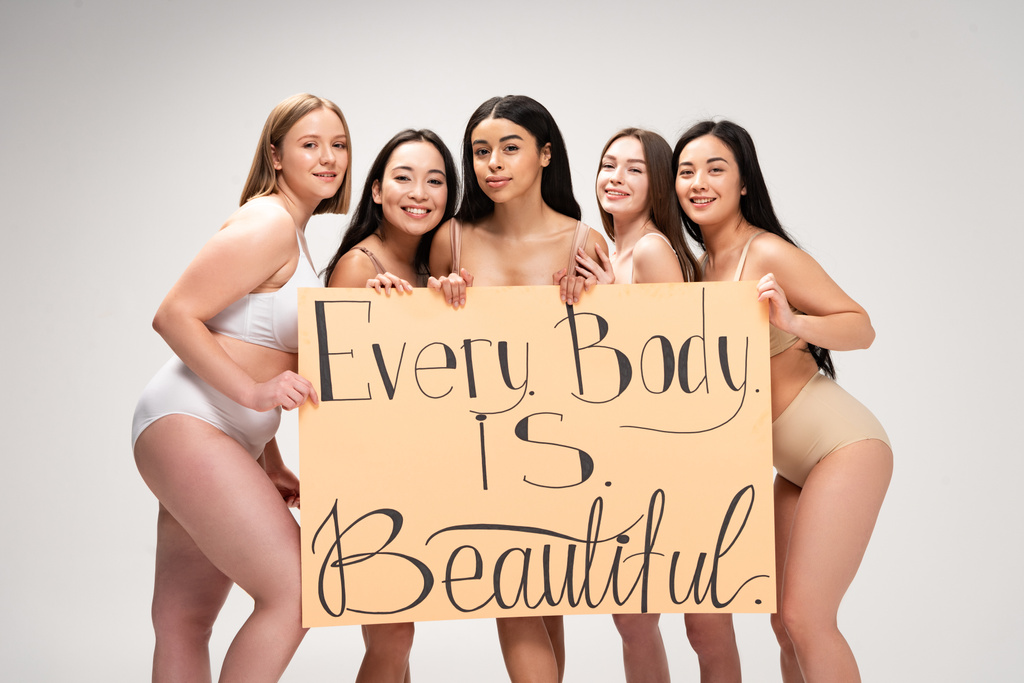πέντε χαμογελαστά κορίτσια πολυεθνική κρατώντας πλακάτ με την επιγραφή «κάθε σώμα είναι όμορφο» που απομονώνονται σε γκρι  - Φωτογραφία, εικόνα