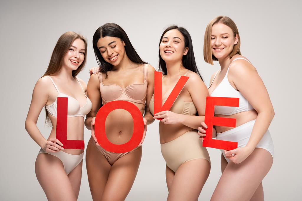 quattro bella giovane donna multietnica in biancheria intima in possesso di carta tagliata parola "amore" isolato su grigio, concetto di positività del corpo
 - Foto, immagini