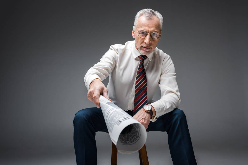 избирательный фокус зрелого бизнесмена в очках, держащего газету на сером
  - Фото, изображение