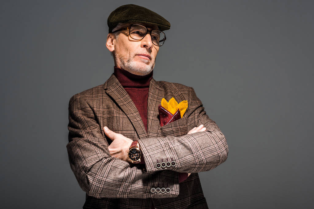 elegante hombre de mediana edad en gafas y gorra de pie con los brazos cruzados en gris
  - Foto, Imagen