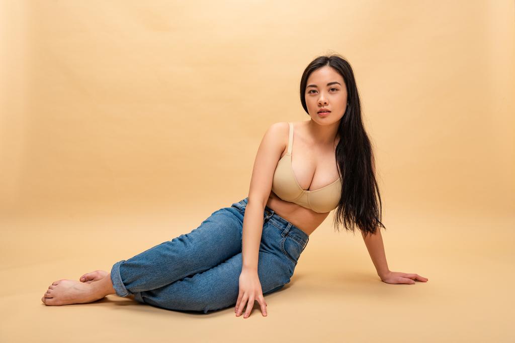 pretty girl in blue jeans and bra sitting and looking at camera, body positivity concept - Photo, Image