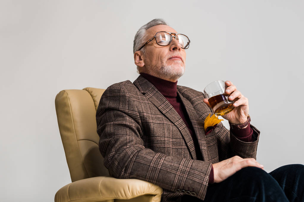 kypsä mies istuu nojatuolissa suljettujen silmien ja pitämällä lasi viskiä eristetty harmaa
 - Valokuva, kuva