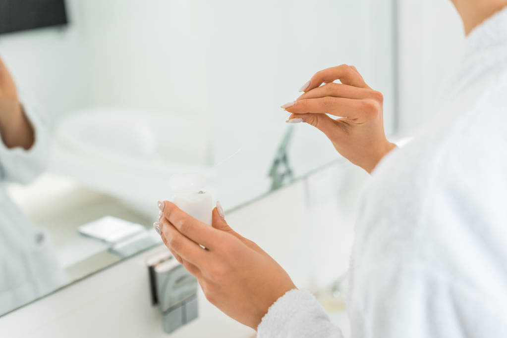 selective focus of young adult woman holding cosmetic cream in bathroom  - Photo, Image
