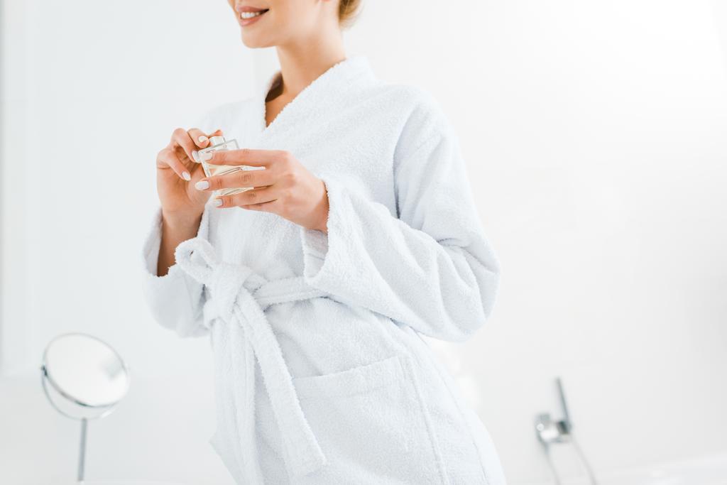 corte vista da mulher em roupão de banho branco segurando perfume no banheiro
  - Foto, Imagem