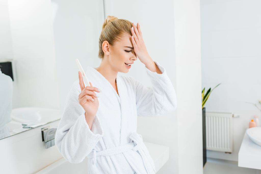 Traurige und blonde Frau im weißen Bademantel mit Nagelfeile im Badezimmer  - Foto, Bild