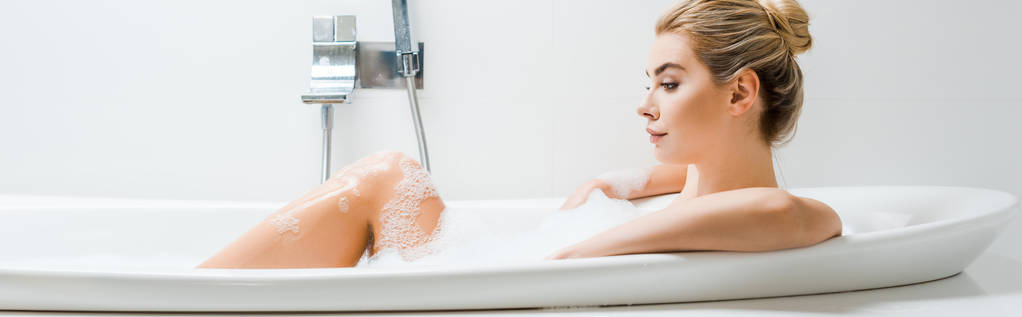 plan panoramique de belle femme blonde prenant un bain avec de la mousse et regardant loin dans la salle de bain
  - Photo, image
