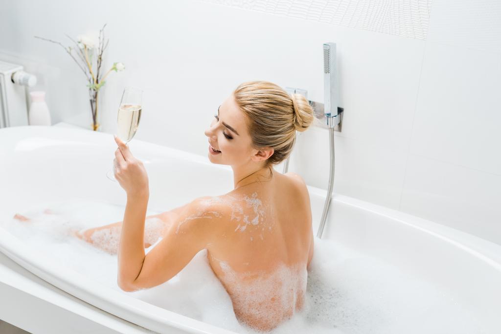 belle et souriante femme prenant bain et tenant verre de champagne dans la salle de bain
  - Photo, image