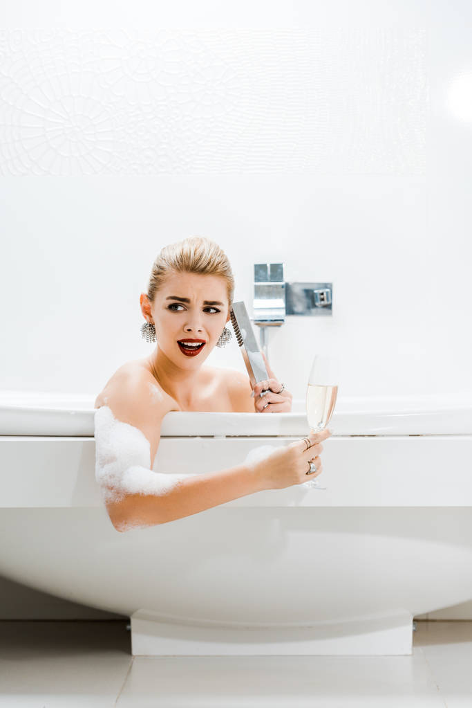 güzel ve sarışın kadın alarak Banyosu, şampanya kadehi tutarak ve banyoda konuşuyor  - Fotoğraf, Görsel
