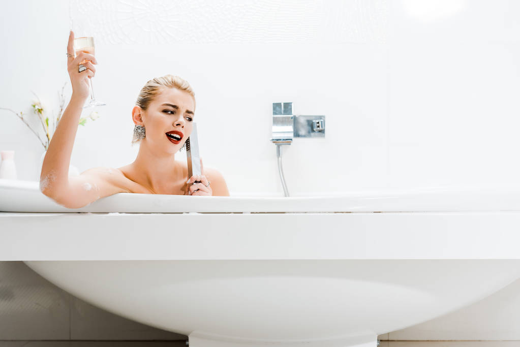 atraktivní a blondýna žena s koupel, drží šampaňské a mluví v koupelně  - Fotografie, Obrázek