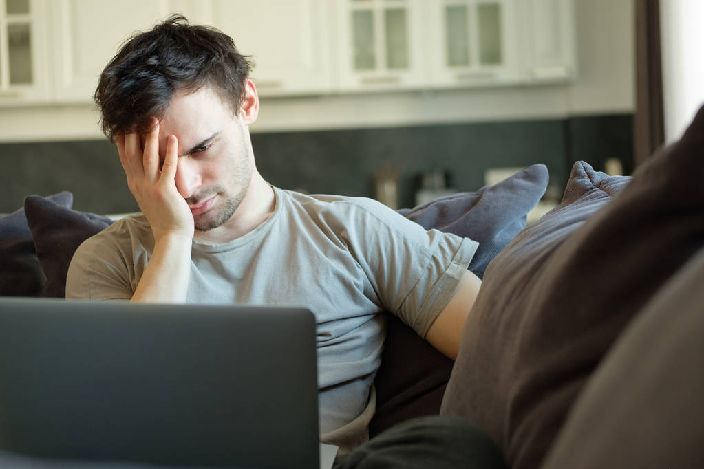 hombre frustrado delante de un ordenador portátil en casa en el sofá
 - Foto, Imagen