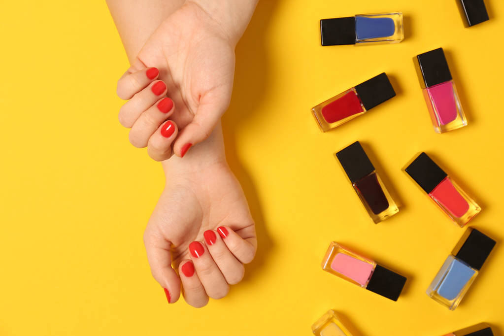 Woman with red manicure and nail polish bottles on color background, top view - Photo, Image