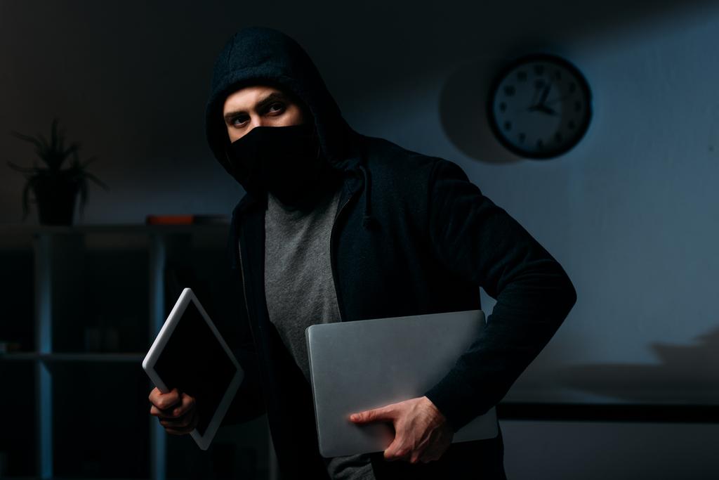 Κλέφτης στη μάσκα κλοπή φορητού υπολογιστή και ψηφιακό tablet και αναζητούν μακριά - Φωτογραφία, εικόνα