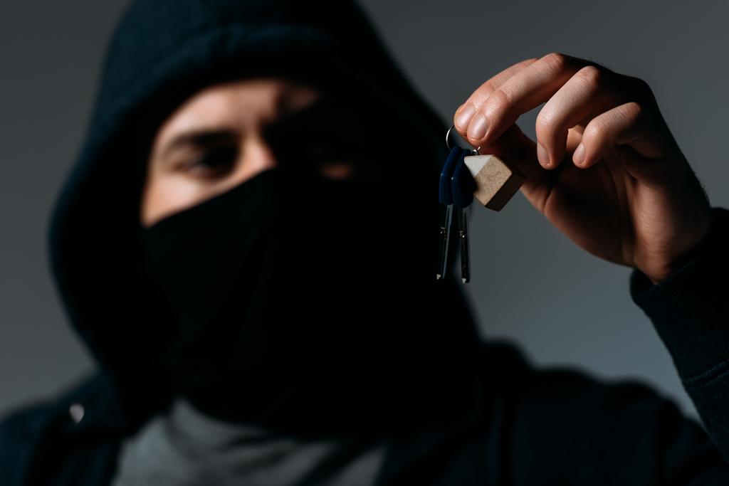 Thief in mask and black hoodie looking at keys on grey - Photo, Image