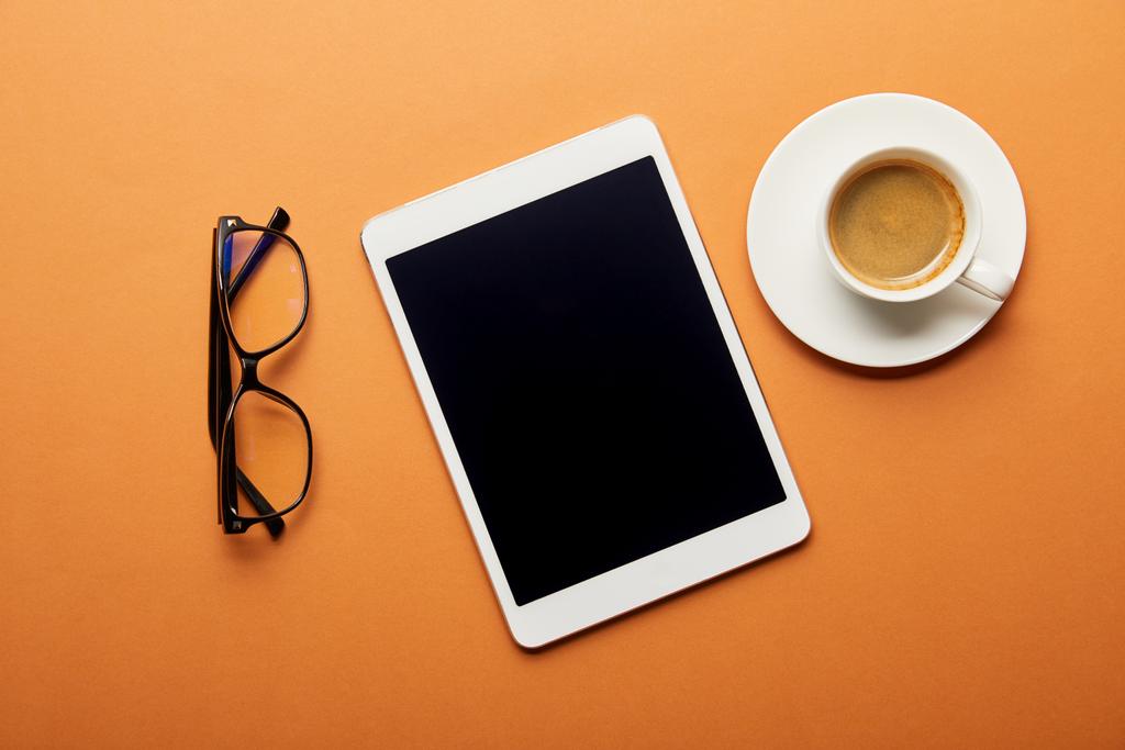 bovenaanzicht van digitale tablet met leeg scherm in de buurt van kopje koffie en glazen op oranje  - Foto, afbeelding