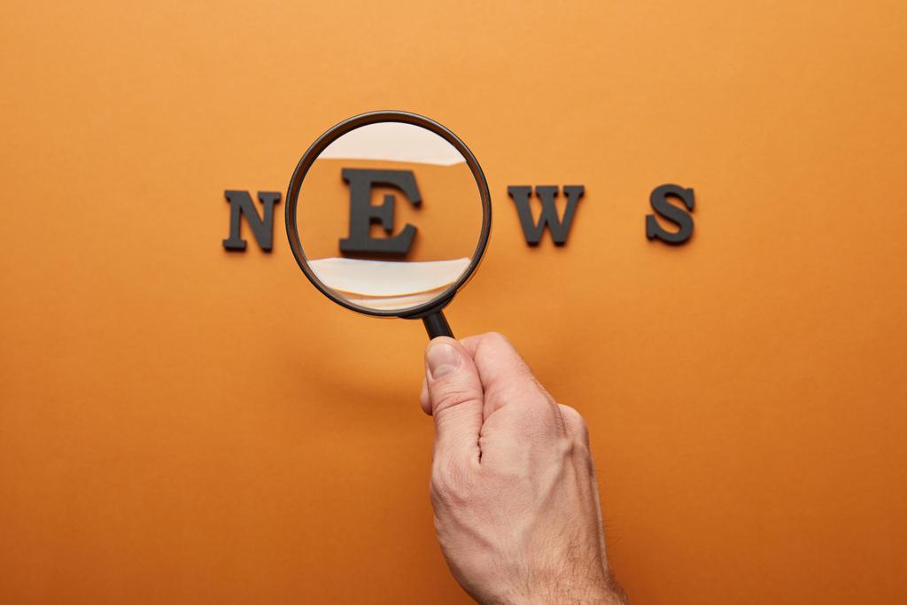 vista recortada del hombre sosteniendo lupa y acercamiento letras de noticias en naranja
  - Foto, Imagen