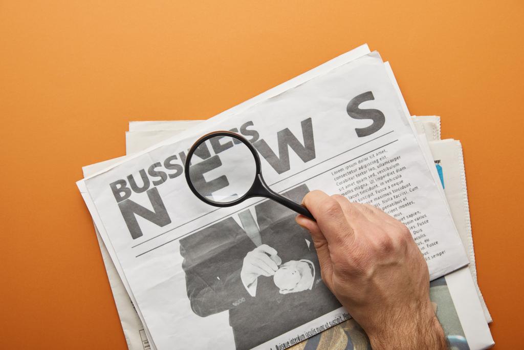 чоловік тримає збільшувальне скло та збільшуючи новини, читаючи бізнес-газети на апельсині
  - Фото, зображення