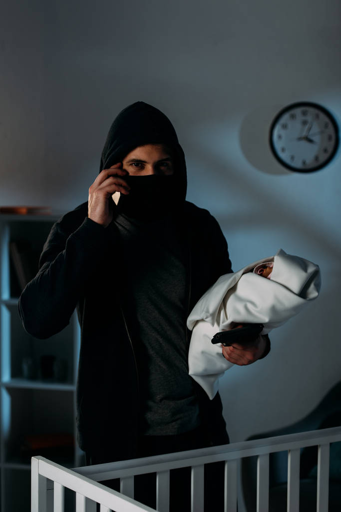 Secuestrador con pistola sosteniendo a un bebé y hablando por teléfono inteligente
 - Foto, imagen