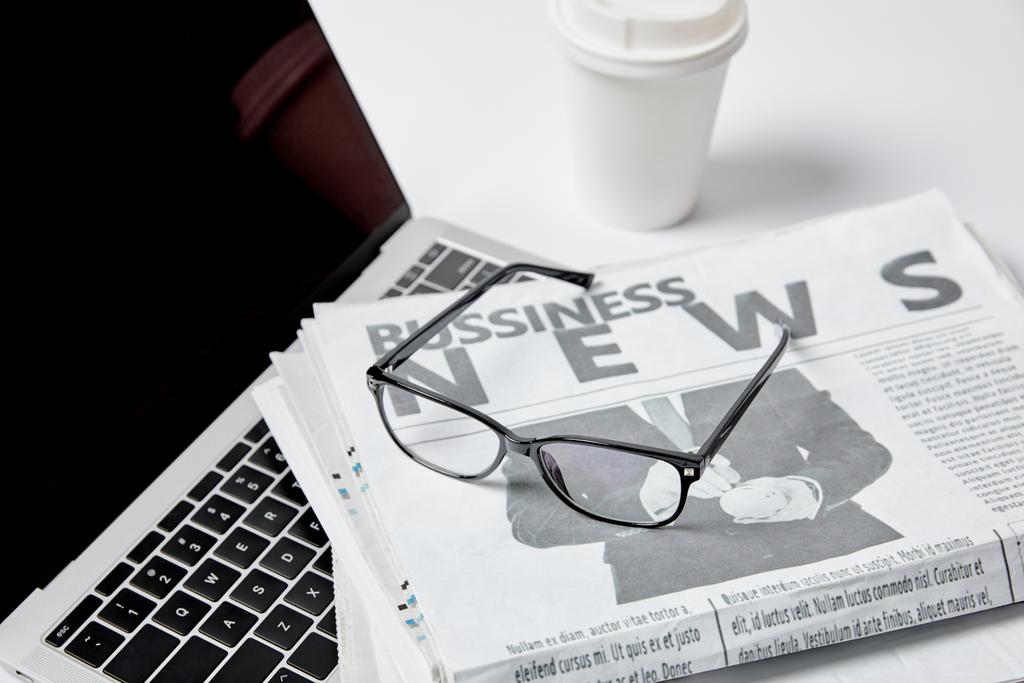 ordinateur portable avec écran blanc près des journaux d'affaires, lunettes, tasse en papier et stylo sur blanc
  - Photo, image