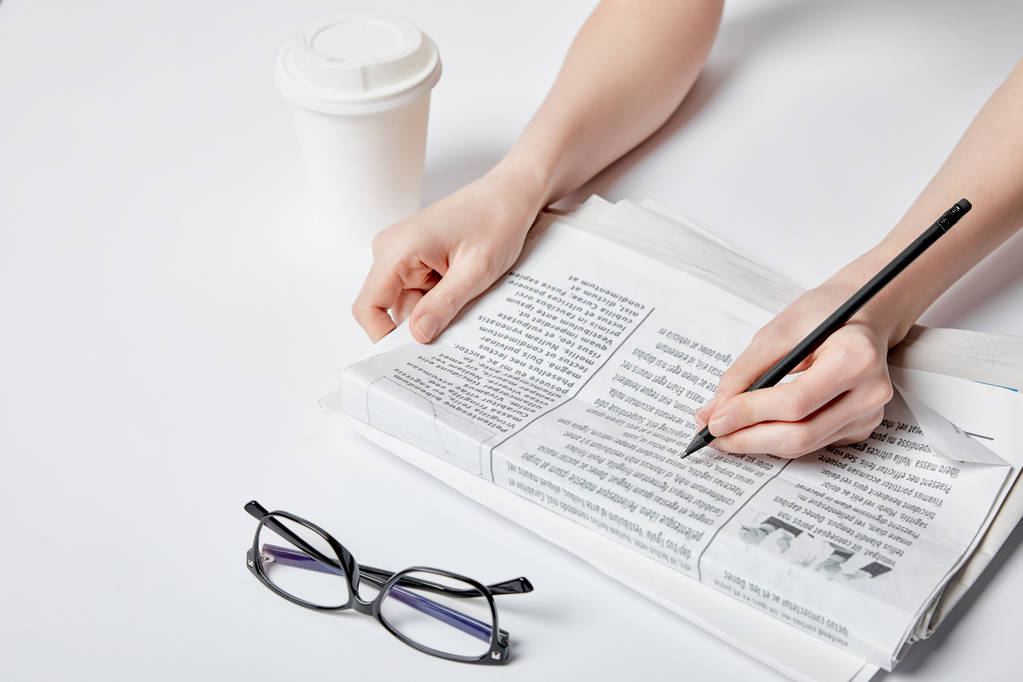 bijgesneden beeld van vrouw met potlood in de buurt van krant, bril en papier cup op wit  - Foto, afbeelding